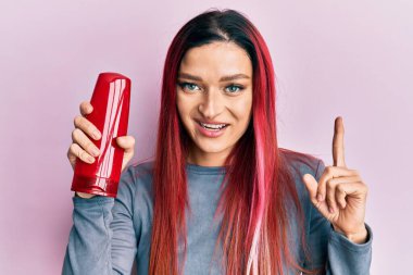 Elinde şampuan şişesi olan genç beyaz bir kadın bir fikirle gülümsüyor ya da bir soru işareti yapıyor. 