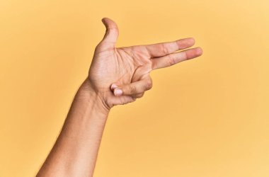 Beyaz adamın kolu ve eli sarı arka planda izole edilmiş. Ateşli silahı parmaklarıyla işaret ediyor, nişan alıyor. 