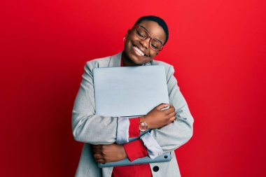 Genç Afro-Amerikan iş kadını elinde dizüstü bilgisayarla mutlu ve havalı bir gülümsemeyle gülümsüyor. diş gösterme. 