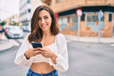Genç İspanyol kadın şehirde akıllı telefon kullanarak mutlu bir şekilde gülümsüyor..