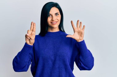 Gündelik giysiler giyen genç beyaz kadın yedi numarayı gösterip işaret ederken kendinden emin ve mutlu bir şekilde gülümsüyor.. 