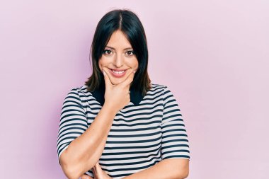 Gündelik kıyafetler giyen genç İspanyol kadın kameraya kendinden emin bakıyor kollarını kavuşturup gülümsüyor ve çenesini kaldırıyor. Olumlu düşünmek. 