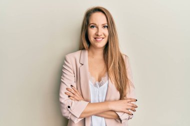 Young blonde woman wearing business jacket and glasses happy face smiling with crossed arms looking at the camera. positive person. 