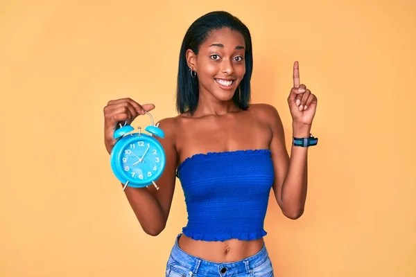 Chica Afroamericana Joven Sosteniendo Despertador Sorprendido Con Una Idea Pregunta —  Fotos de Stock