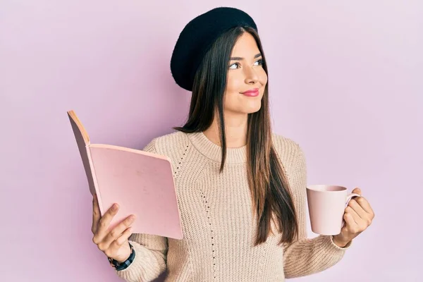 若いですブルネット女性読書本とコーヒーを飲んで笑顔のカップを横に見て 離れて考えて見つめて — ストック写真