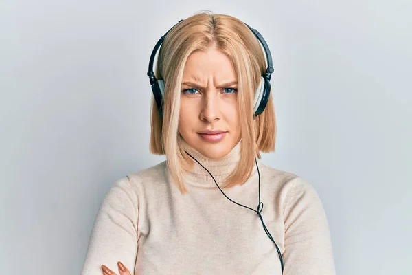 ヘッドフォンを使用して音楽を聴いている若いブロンドの女性は懐疑的で緊張し 両腕を組んで顔の表現を否定しています 否定的な人 — ストック写真