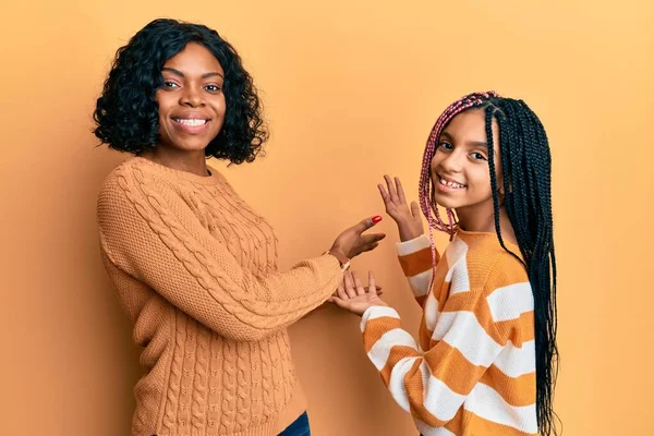 美丽的非洲裔美国母亲和女儿穿着羊毛冬季毛衣 带着开放的手 自然地笑着走进来 — 图库照片