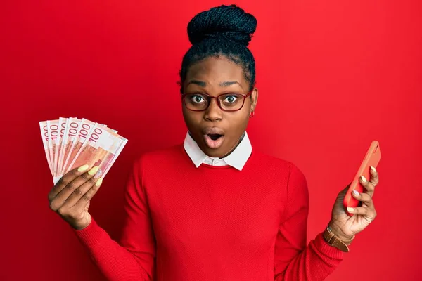Joven Mujer Afroamericana Usando Smartphone Sosteniendo Billetes Noruegos Asustada Conmocionada —  Fotos de Stock