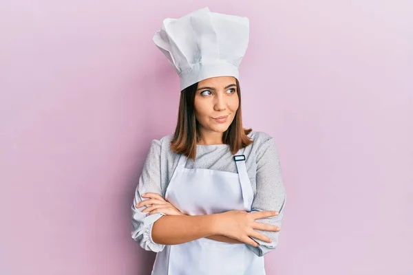 年轻漂亮的女人穿着职业厨师的制服 戴着帽子 面带微笑地望着旁边 望着远方 想着心事 — 图库照片