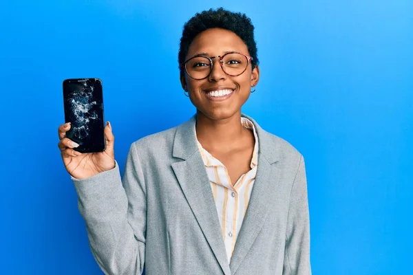 Young african american girl holding broken smartphone showing cracked screen looking positive and happy standing and smiling with a confident smile showing teeth