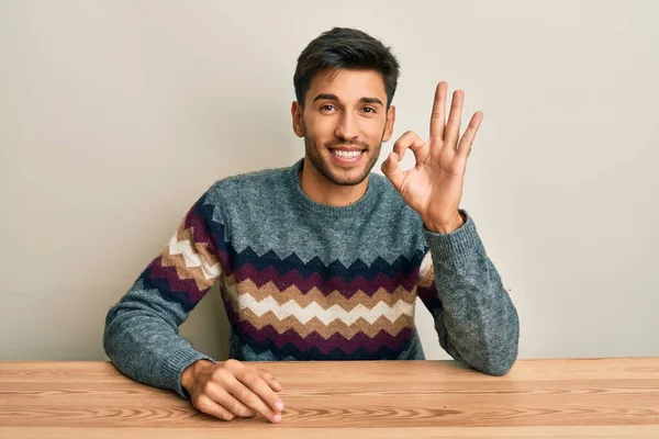 스웨터를 테이블에 긍정적으로 웃으며 손가락으로 괜찮은 사인을 잘생긴 성공적 — 스톡 사진