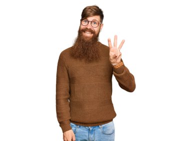 Genç İrlandalı kızıl elbiseli ve gözlüklü adam üç numaralı parmaklarını gösterip işaret ederken kendinden emin ve mutlu gülümsüyor.. 