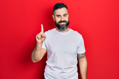 Günlük beyaz tişört giyen genç İspanyol bir adam bir fikir ya da soruyla gülümsüyor ve mutlu bir yüzle işaret ediyor. 