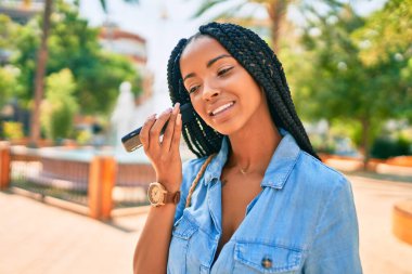 Genç Afrikalı Amerikalı kadın gülümsüyor. Parktaki akıllı telefondan mutlu bir şekilde sesli mesaj dinliyor..