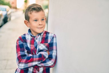 Kollarını kavuşturup gülümseyen sevimli beyaz çocuk şehrin duvarına yaslanmış mutlu..