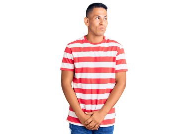 Genç, yakışıklı, gündelik kıyafetler giyen, gülümseyen, yan bakan ve düşünen Latin bir adam.. 