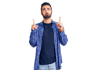 Gündelik kıyafetler giyen genç İspanyol adam üzgün ve üzgün görünüyor, parmaklarıyla yön gösteriyor, mutsuz ve depresif.. 