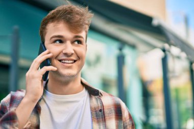 Genç beyaz adam gülümsüyor. Şehirdeki akıllı telefondan konuşuyor..