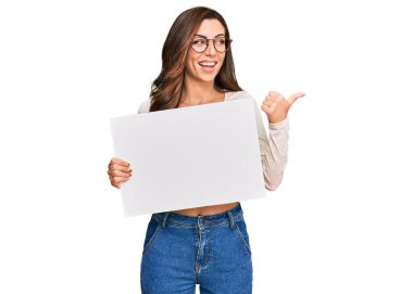 Boş afiş taşıyan genç esmer kadın başparmağını yana kaldırmış, ağzı açık gülümsüyor. 