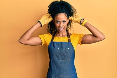 Orta yaşlı Afro-Amerikalı kadın profesyonel önlük giyiyor gülümsüyor kulakları parmaklarıyla çekiyor, komik bir jest. deneme sorunu 