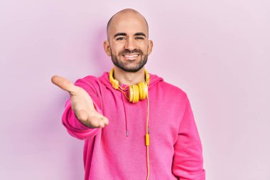 Spor kıyafetleri giyen, kulaklık takan, dostça gülümseyen ve selamlaşan genç kel bir adam. başarılı iş. 