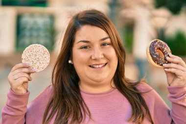 Genç İspanyol artı iri kadın gülümseyerek şehirde pirinç keki ve çörek tutuyor..