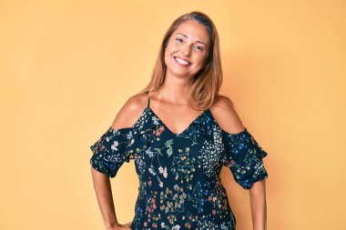 Orta yaşlı İspanyol kadın gündelik kıyafetler giyiyor. Pozitif ve mutlu görünüyor. Kendine güvenen bir gülümsemeyle dişlerini gösteriyor. 