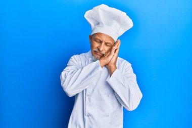 Orta yaşlı, gri saçlı, profesyonel aşçı üniforması giyen, şapkası olan, yorgun uyuyan, hayal kuran, elleriyle poz veren ve gözleri kapalı gülümseyen bir adam.. 