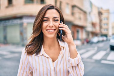 Genç İspanyol kadın gülümsüyor. Şehirdeki akıllı telefondan konuşuyor..