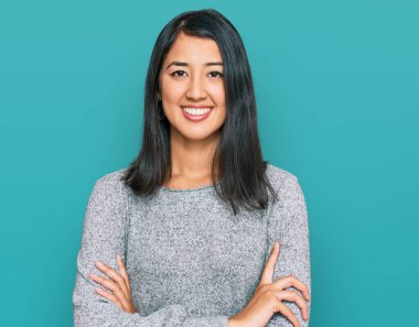 Sıradan kıyafetler giyen güzel Asyalı genç bir kadın kollarını kavuşturup kameraya bakarken gülümsüyor. pozitif kişi. 