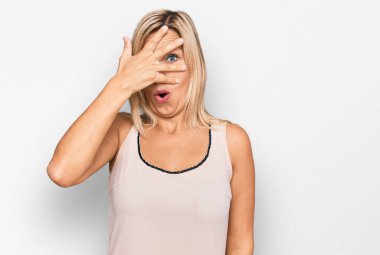 Orta yaşlı beyaz kadın, günlük kıyafetler giyip, şok içinde yüzünü ve gözlerini kapayarak utangaç ifadesiyle parmaklarının arasından bakıyor.. 