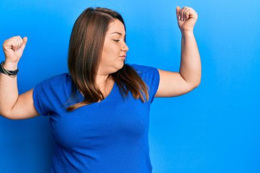 Güzel esmer, iri yarı, sıradan mavi tişört giyen, gururla gülümseyen kol kaslarını gösteren bir kadın. fitness konsepti. 