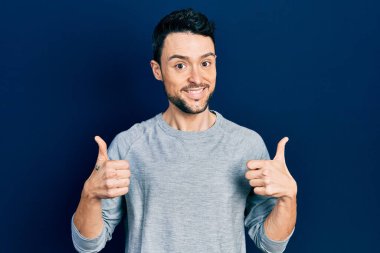 Gündelik kıyafetler giyen genç İspanyol adam. Başarı işareti yapıyor. Elleriyle olumlu jest yapıyor. Neşeli ifade ve kazanan jest. 