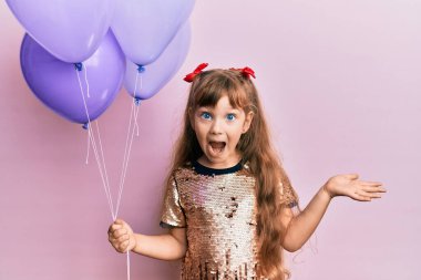 Küçük beyaz kız elinde balonlarla başarıyı mutlu bir gülümsemeyle kutluyor ve kazanan el kaldırarak ifade ediyor. 