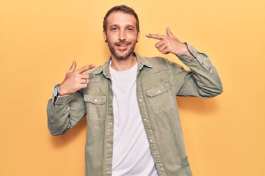 Gündelik kıyafetler giyen, neşeli gülümseyen, parmaklarıyla ve ağzıyla işaret eden genç yakışıklı bir adam. diş sağlığı kavramı. 