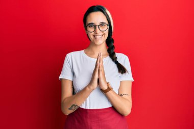 Profesyonel garson önlüğü giyen genç İspanyol kadın ellerinin birarada dua ederek af diliyor kendinden emin bir şekilde gülümsüyor.. 