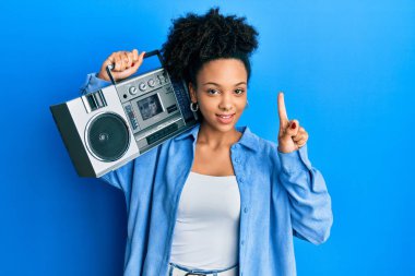 Genç Afrikalı Amerikalı bir kız elinde teyp ile bir fikir ya da soru işareti ile gülümseyen müzik dinliyor. 