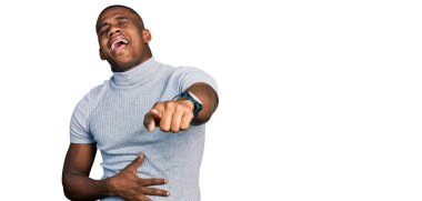 Gündelik tişört giyen genç siyah bir adam sana gülüyor, eli vücudunun üzerinde kamerayı işaret ediyor, utanç ifadesi. 