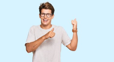 Yakışıklı beyaz adam, günlük kıyafetler ve gözlük takıyor. Arka tarafı işaret ediyor. El ve baş parmakları havada, kendinden emin. 