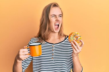 Güzel sarışın kadın donut yiyor ve kahve içiyor kızgın ve öfkeli çığlıklar atıyor öfkeyle bağırıyor. öfke ve agresif konsept. 