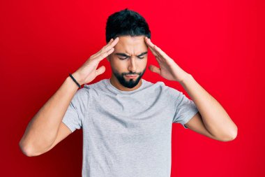 Sakallı genç adam, elleri kafasında, günlük beyaz tişört giyiyor, stresten baş ağrısı çekiyor. migren ağrısı. 