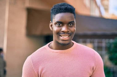 Genç Afrikalı Amerikalı adam gülümseyerek şehirde mutlu mesut duruyor..