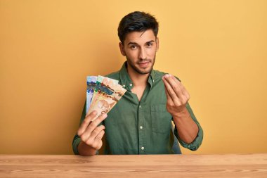 Kanada doları tutan yakışıklı genç adam. Elleriyle jest yapıyor. Maaş istiyor. 
