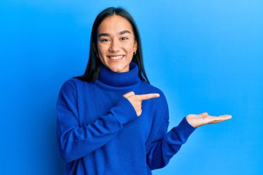 Günlük kışlık süveter giyen genç Asyalı kadın kameraya hayret ediyor ve gülümsüyor.. 