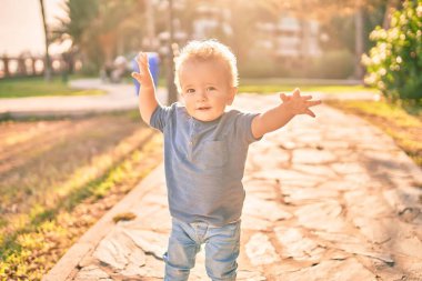 Sevimli ve mutlu küçük çocuk güneşli bir günde parkta eğleniyor. Güzel sarı saçlı erkek çocuk dışarıda oynuyor.