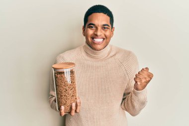 Genç, yakışıklı İspanyol adam elinde sağlıklı tahıl gevreği kavanozuyla gururla bağırıyor zaferi ve başarıyı kutluyor. 