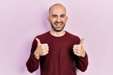 Genç kel bir adam günlük kıyafet giyer başarı işareti yapar. Elleriyle olumlu jest yapar. Gülümser ve mutlu olur. Neşeli ifade ve kazanan jest. 