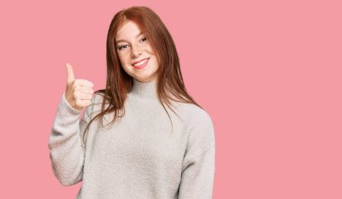 Kış süveteri giyen, neşeli ve pozitif gülümseyen, başparmağıyla mükemmel ve onay işareti yapan genç okumuş kadın. 