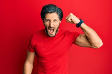 Genç, İspanyol asıllı, normal kırmızı tişört giyen kızgın, kızgın, yumruğunu kaldıran öfkeli ve öfkeyle bağıran bir adam. öfke ve agresif konsept. 