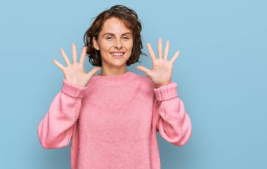 Genç İspanyol kadın gündelik giysiler giyer ve parmaklarını on numara ile gösterir ve gösterirken kendinden emin ve mutlu gülümser.. 